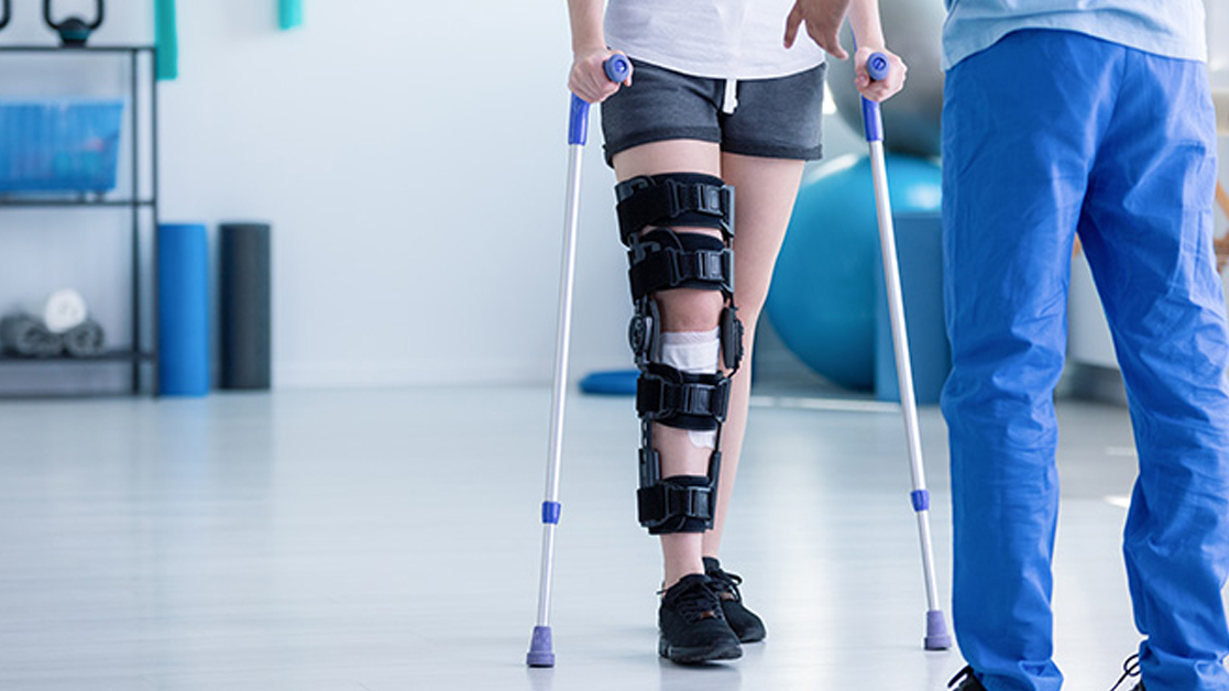 Bottom half of patient in a leg brace standing in a medical facility, facing healthcare professional