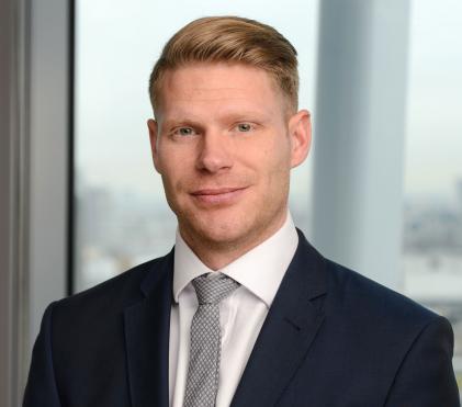 Photo of man wearing suit with fair hair and eyes smiling, grey tie