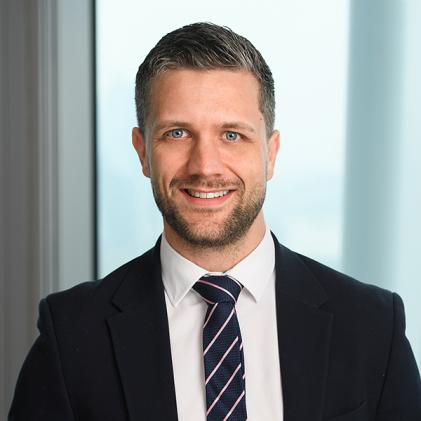 Man with short hair, black suit, white and black tie, beard, smiling