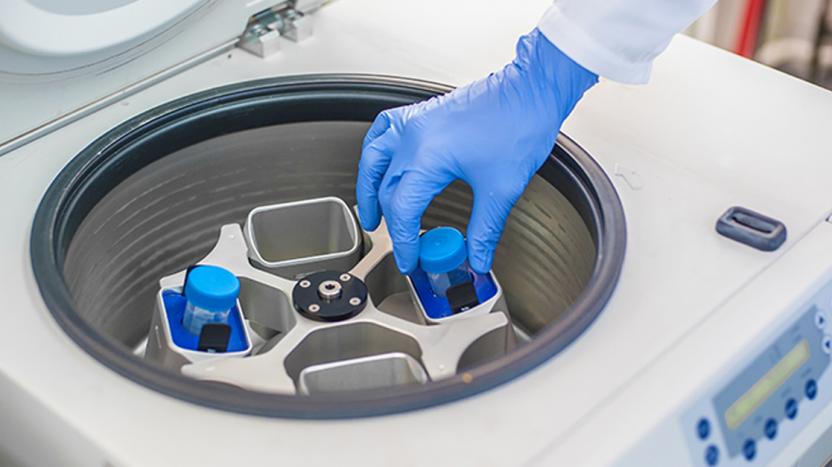 Gloved hand loading a sample into a centrifuge machine